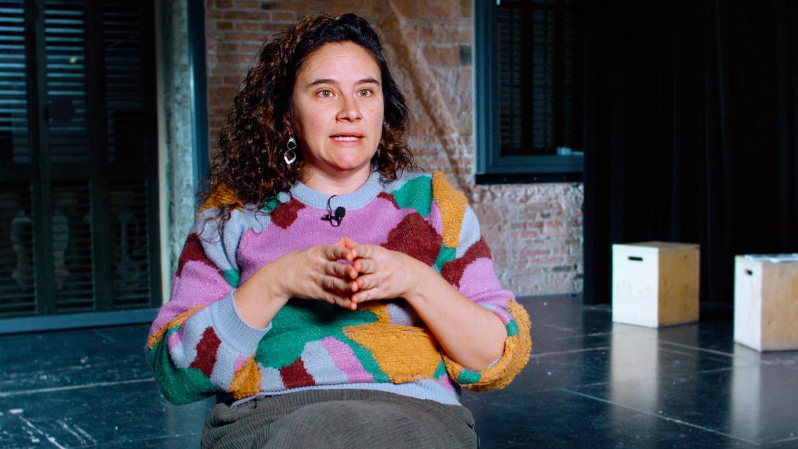 Se ve a Irene González Pijuan en un fotograma de la entrevista con las manos juntadas. Lleva un jersey de colores, detrás se ve una ventana, a su izquierda, con la noche ya caida.